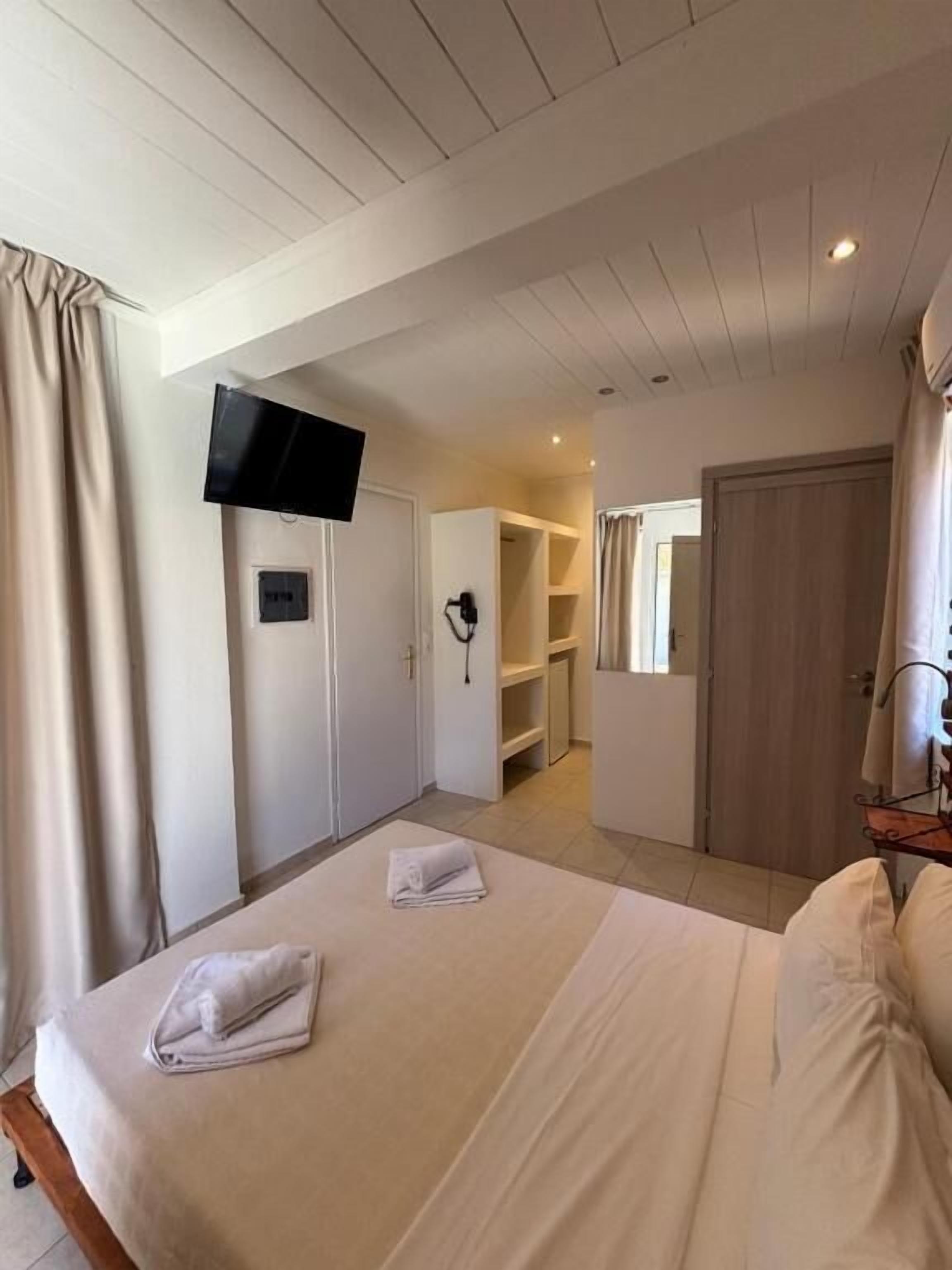 A bedroom with a bed, a TV mounted on the wall, a closet, and a bathroom visible through an open door.
