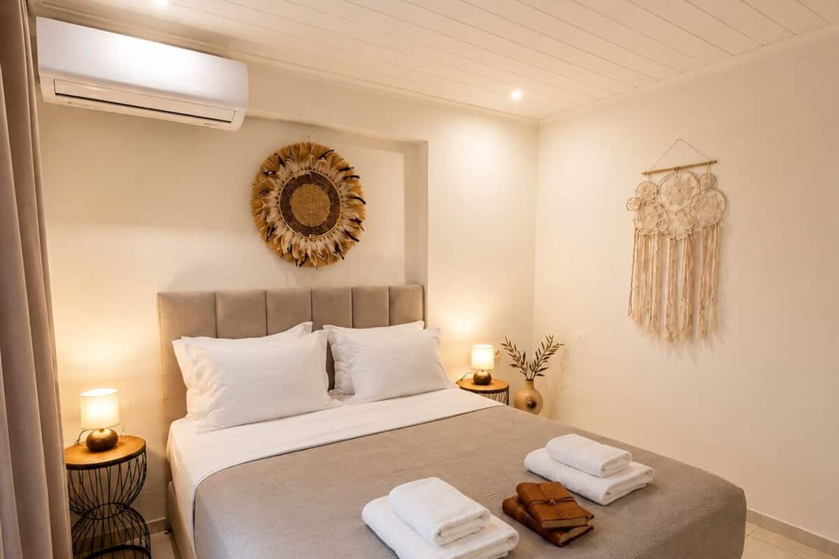 Una cama bien hecha con sábanas blancas, cabecera y aire acondicionado de pared.