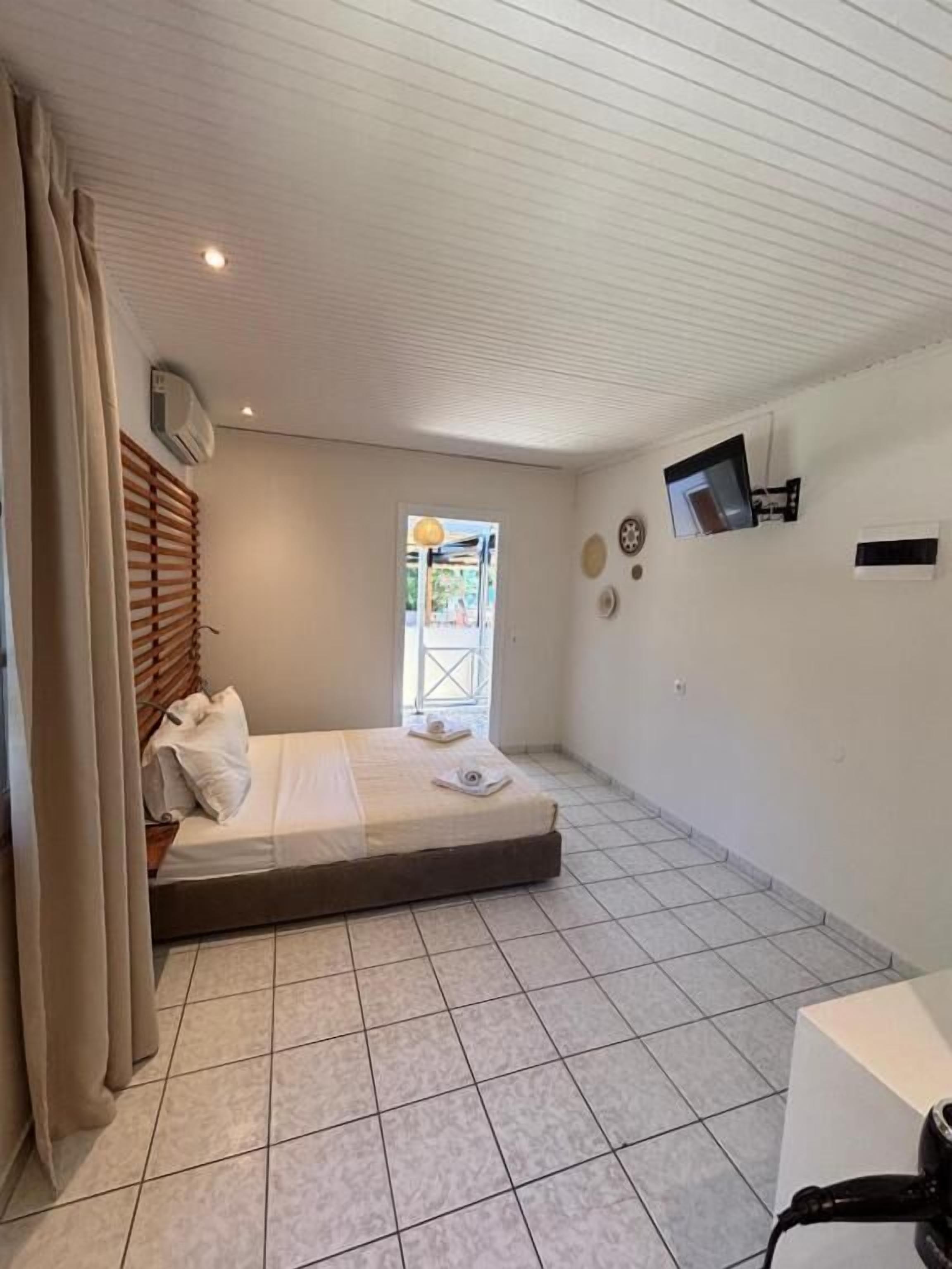A small, clean room with a bed, a TV, and a window.