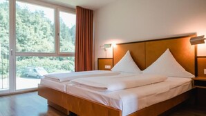 Una cama doble con cabecera de madera, una mesita de noche con lámpara y un ventanal con cortinas.