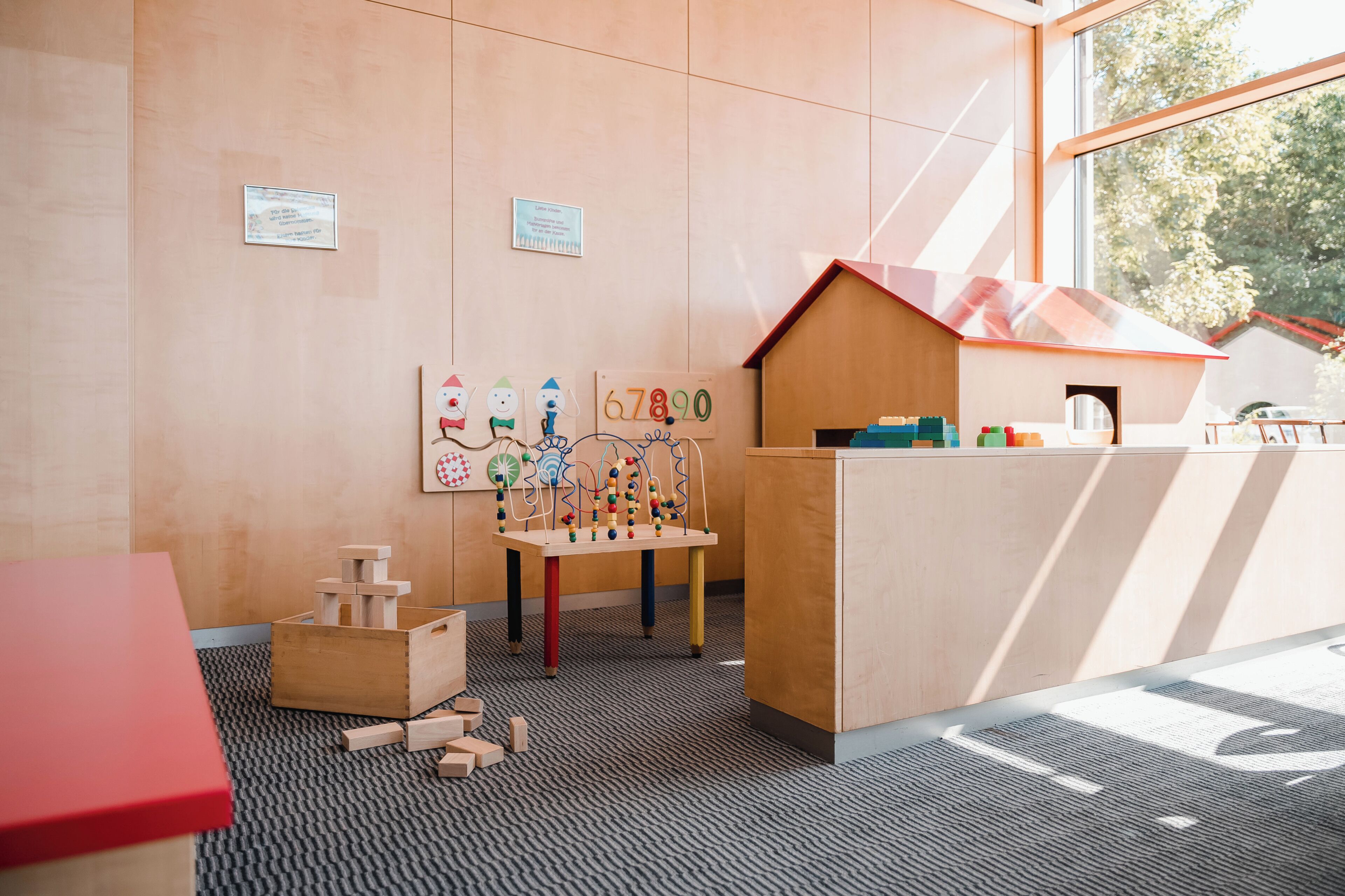 A children's play area with wooden toys, a playhouse, and educational wall decorations.