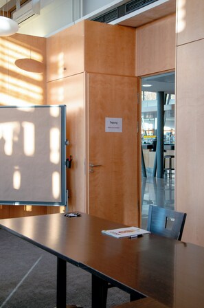 Una sala de conferencias con una mesa de madera, una pizarra y una puerta con la etiqueta 'Tagung'.