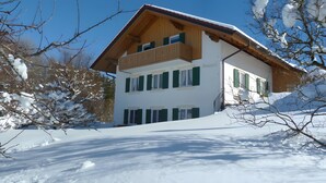 Eine zweistöckige Holzchalet mit Balkon, umgeben von schneebedeckten Bäumen.