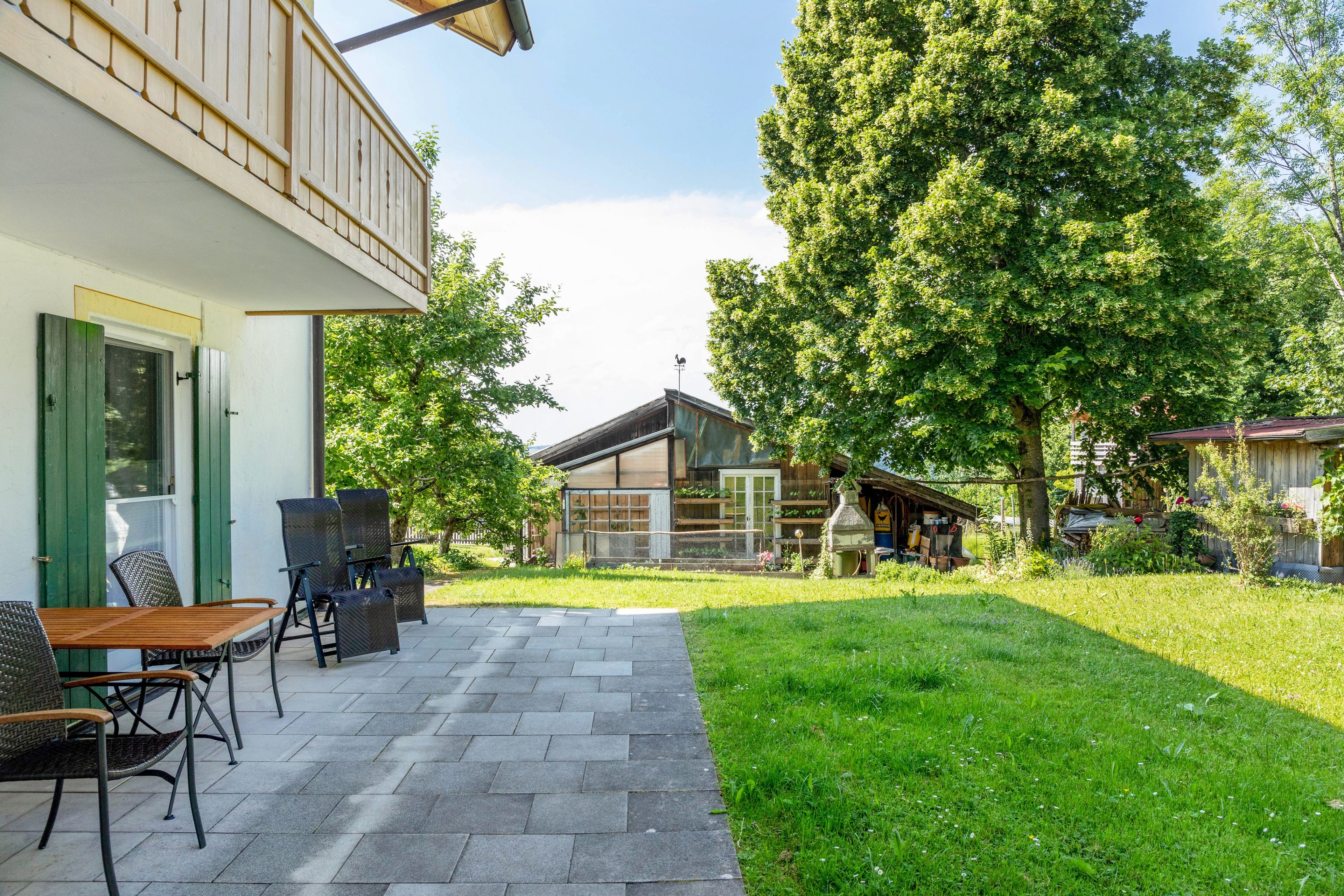 A patio with outdoor furniture, a wooden deck, and a grassy area with trees.