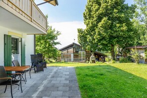 Een terras met buitenmeubilair, een houten dek en een gazon met bomen.