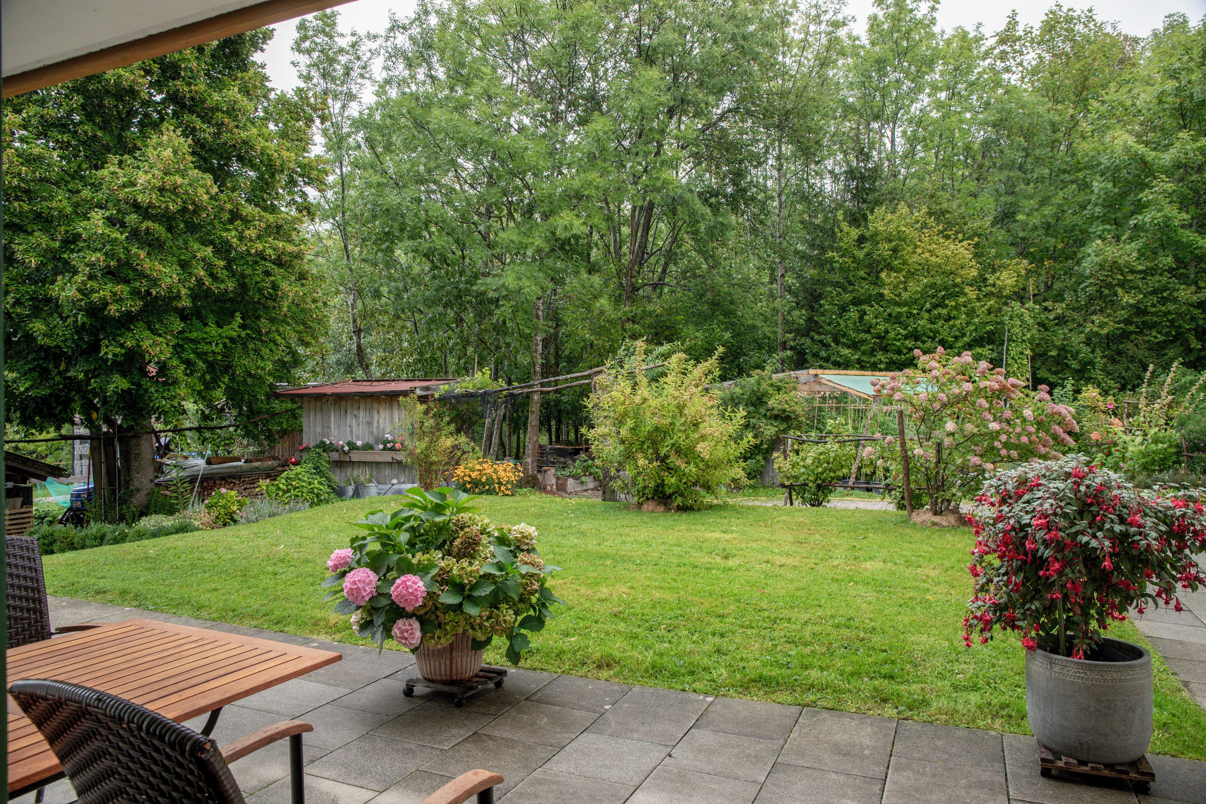 Un'area patio con tavolo e sedie in legno, un prato verde e diverse piante in vaso.