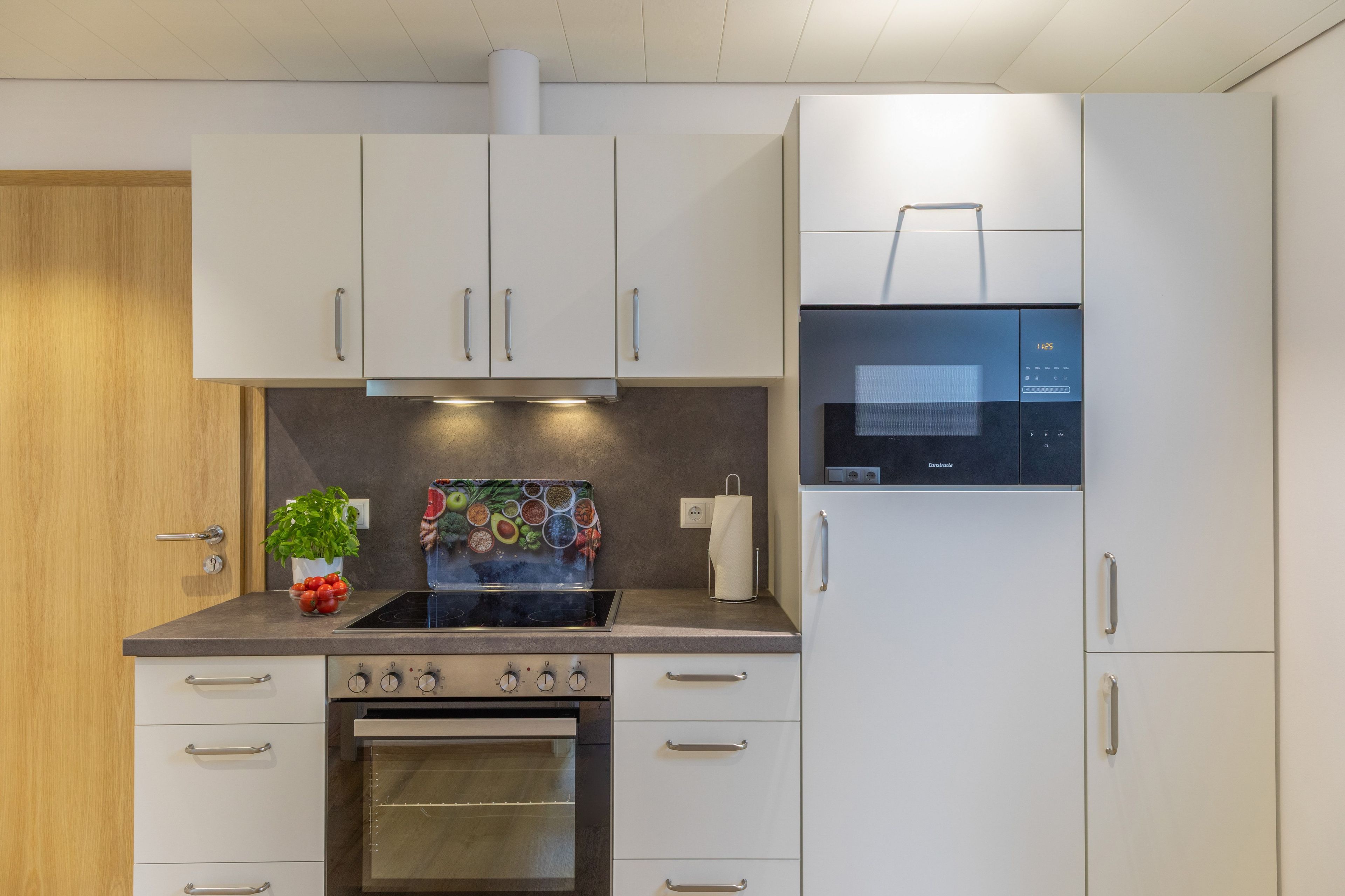 A modern kitchen with white cabinets, a built-in oven, a microwave, and a stove.