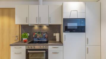 A modern kitchen with white cabinets, a built-in oven, a microwave, and a stove.