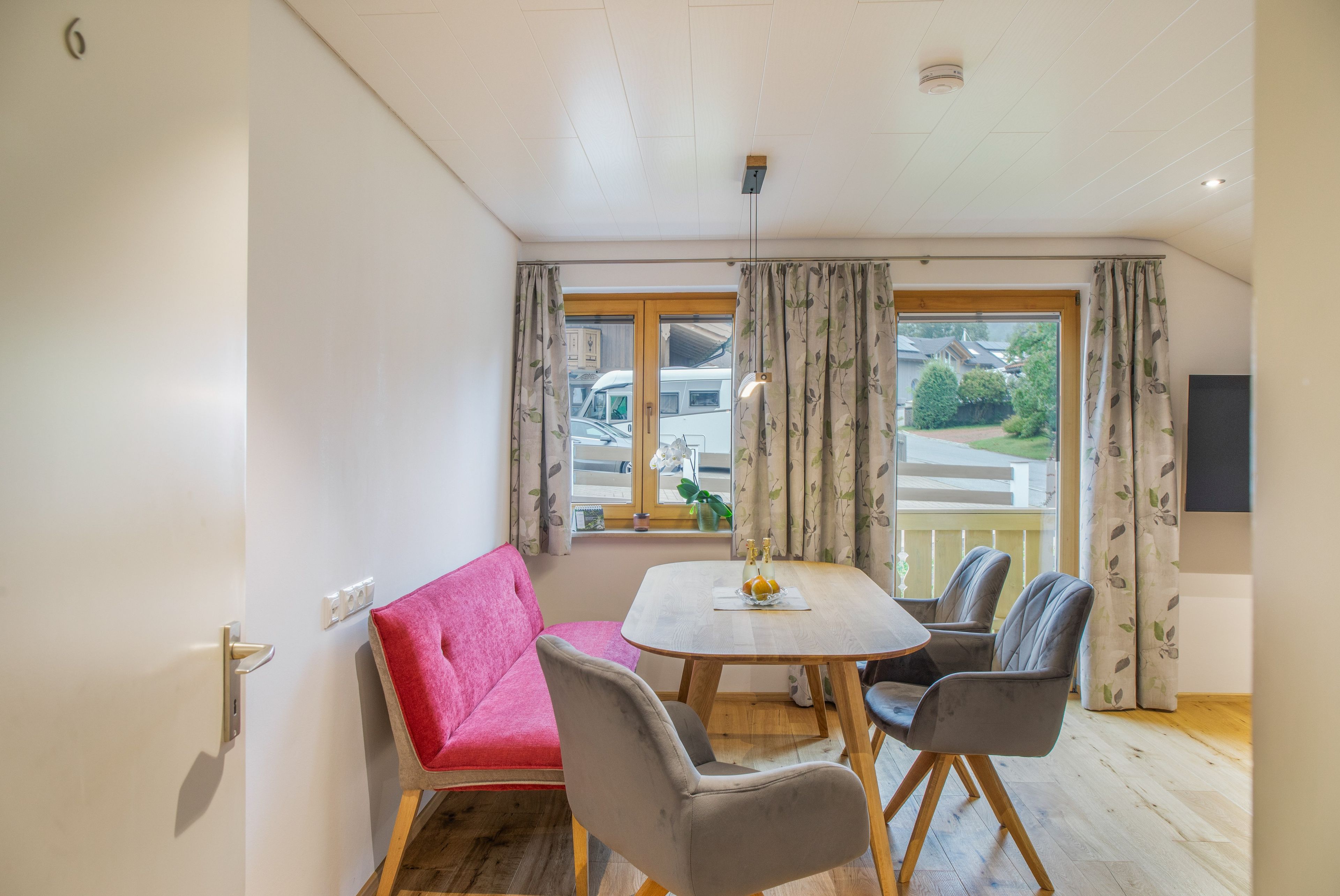 A room with a dining table, two chairs, a sofa, and a window with curtains.