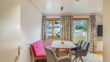 A room with a dining table, two chairs, a sofa, and a window with curtains.