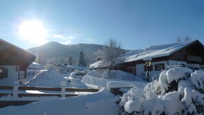 Ein schneebedecktes Dorf mit Holzhäusern, einem Holzzaun und Bergen im Hintergrund.