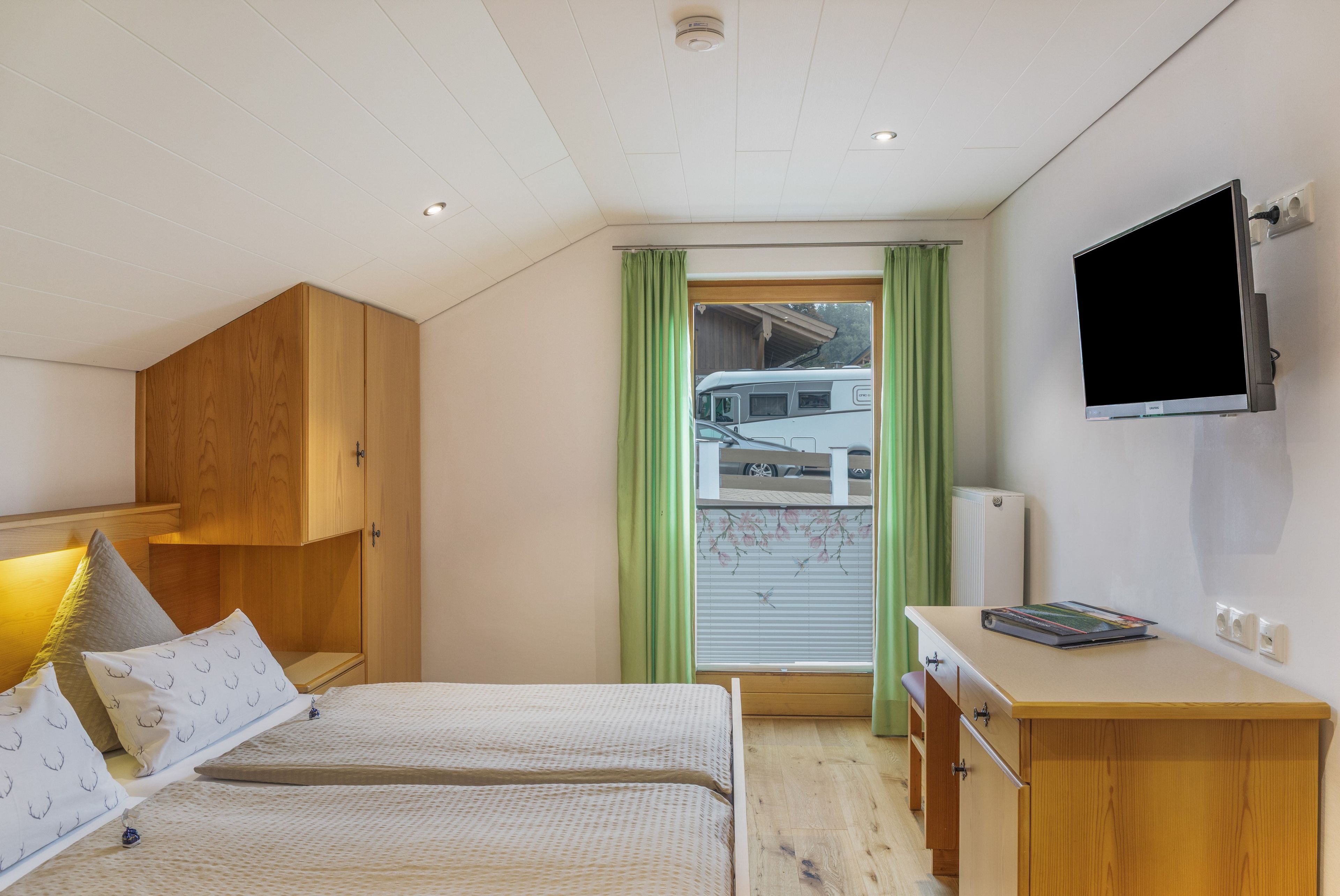 Une chambre avec deux lits, une armoire en bois, un bureau avec un téléviseur à écran plat et une fenêtre donnant sur un camping-car.