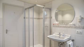 Et moderne badeværelse med brusekabine i glas, et håndvaskarrangement med spejl og toiletartikler på bordet.