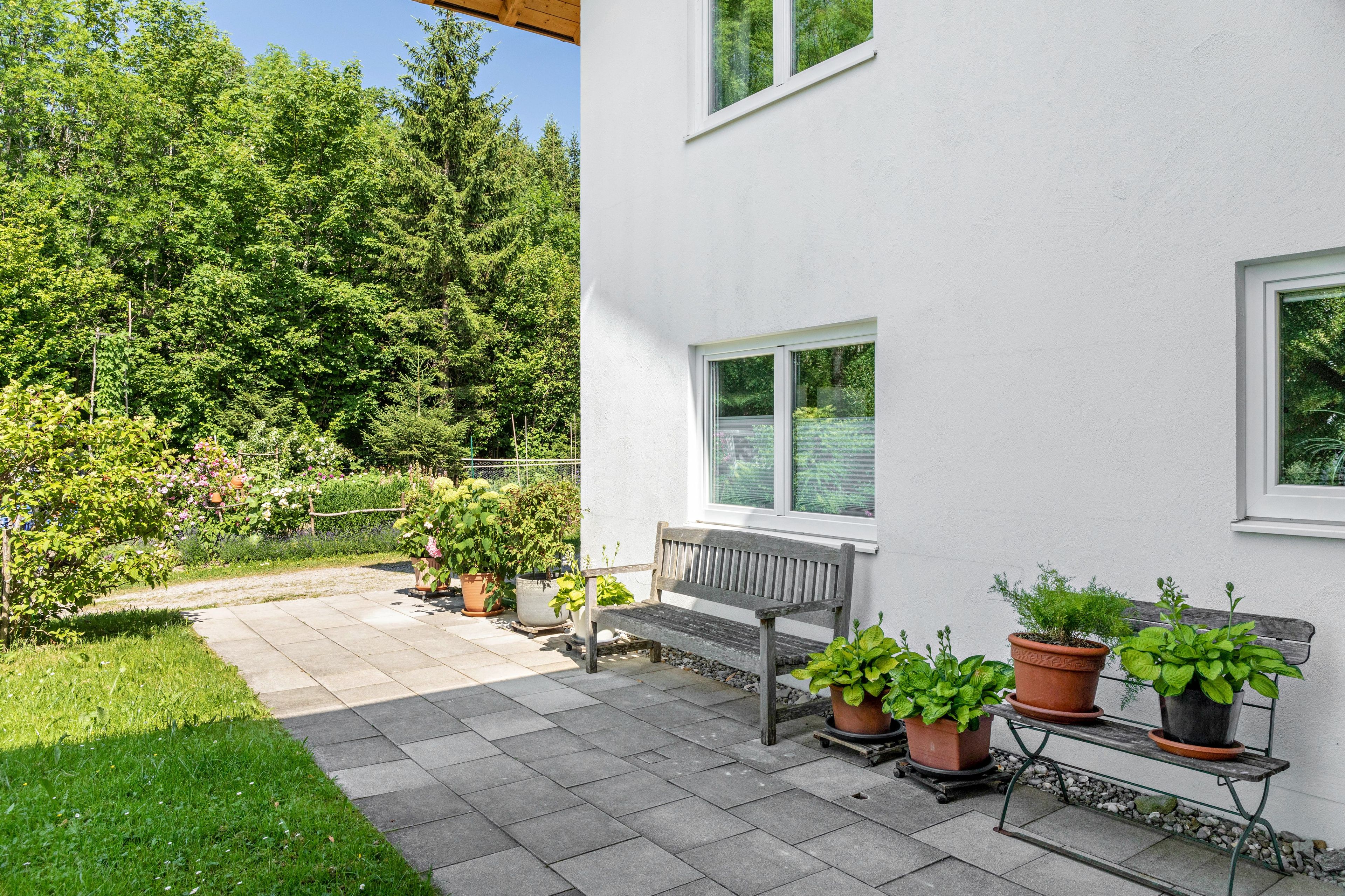 A patio with a bench, potted plants, and a view of a forest.
