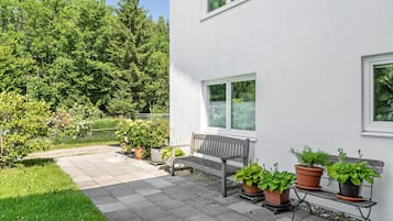 A patio with a bench, potted plants, and a view of a forest.