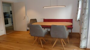 A dining area with a wooden table, grey chairs, a red bench, and a pendant light. - Apartment “Anna” with Mountain View, Shared Terrace, and Wi-Fi (Bad Kohlgrub)