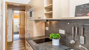 Een moderne keuken met houten kastjes, een ingebouwde oven, een zwart inductiekookveld, een spoelbak en hangend keukengerei.