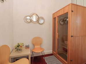 Ein Zimmer mit einem Holzkasten, einem Tisch mit Stühlen, einer Vase mit Blumen und Wandspiegeln.