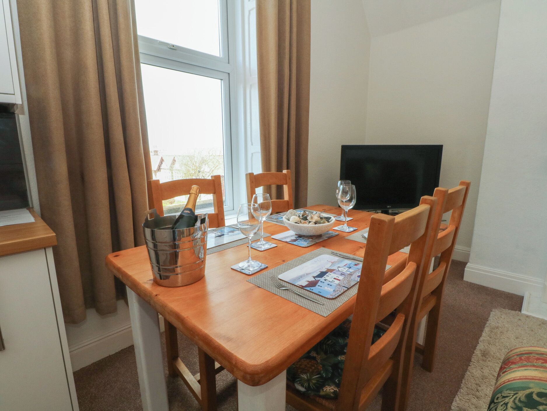 A dining area with a wooden table, chairs, a TV, and a window with curtains.