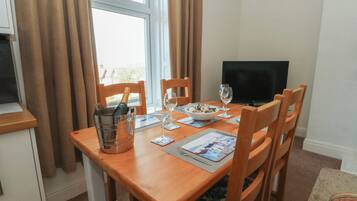 A dining area with a wooden table, chairs, a TV, and a window with curtains.