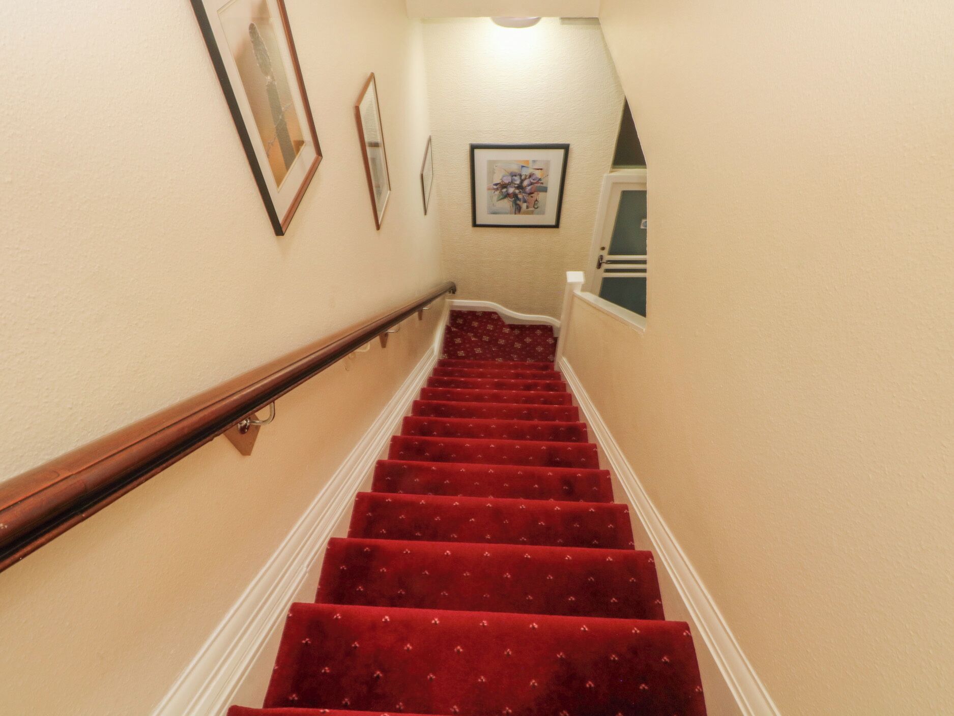 A staircase with red carpeted steps, wooden handrails, and beige walls.