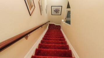 A staircase with red carpeted steps, wooden handrails, and beige walls.