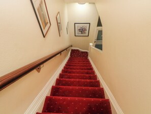 A staircase with red carpeted steps, wooden handrails, and beige walls. - Apartment 3 (Lytham St. Anne's)