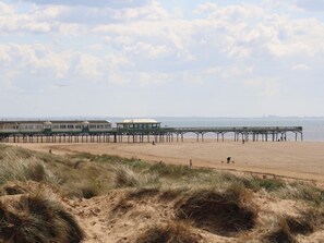 A beach with a pier extending into the water, sandy dunes in the foreground, and a clear sky. - Apartment 3 (Lytham St. Anne's)
