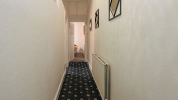 A narrow hallway with patterned carpet, white walls, and a radiator.