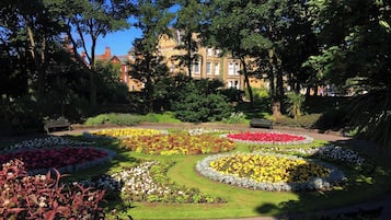 A garden with flower beds and benches, surrounded by trees and a building in the background.