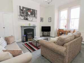 A living room with a fireplace, sofa, television, and a dining area with a table and chairs. - Apartment 2 (Lytham St. Anne's)