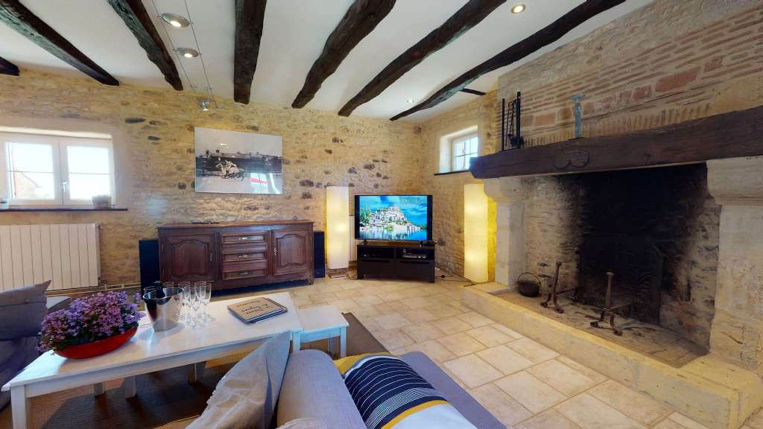 A rustic living room with exposed beams, a stone wall, a fireplace, a television, and a sofa.