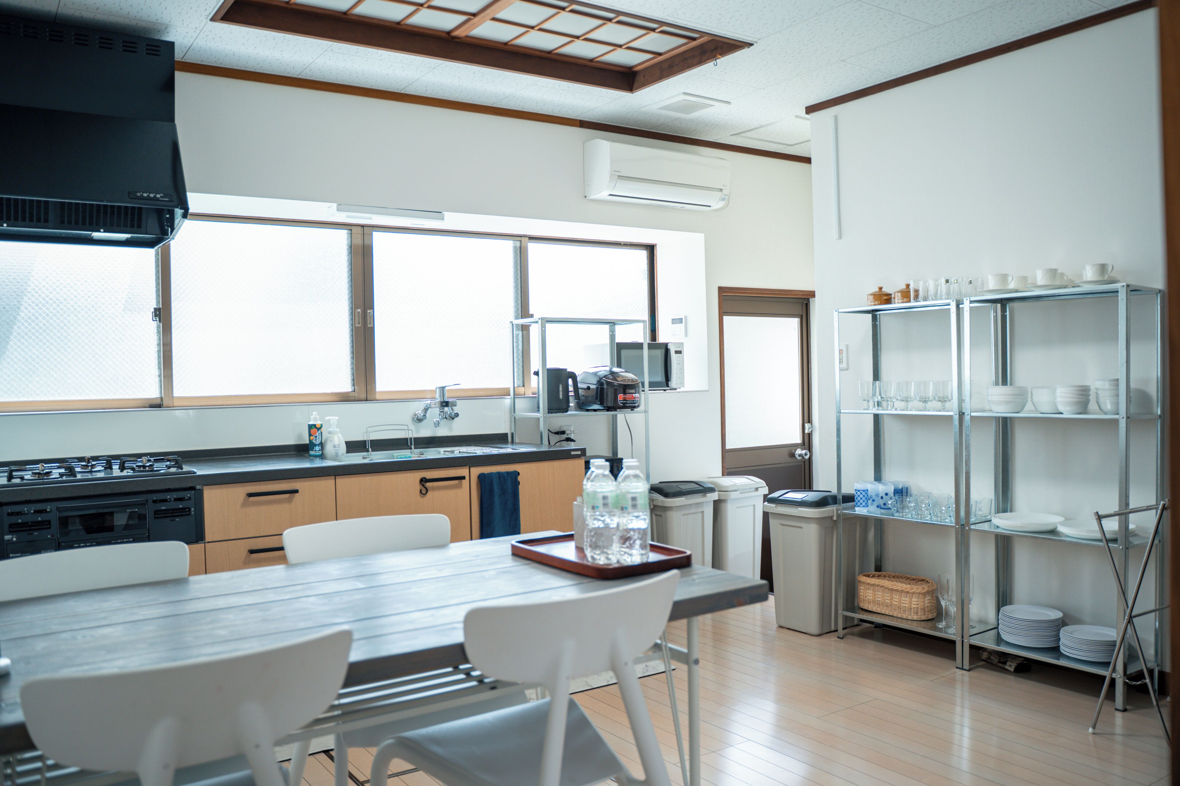 A modern kitchen with a dining area, featuring a stove, sink, and a shelf with dishes.