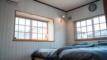 Une pièce avec deux fenêtres, un lit, une horloge murale et une lampe.