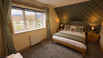 Quarto com cama, radiador, janela com cortinas, parede estampada e mesa de cabeceira com abajur.
