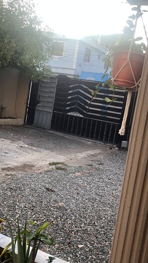 A gated area with a gravel driveway, a metal gate, and a building in the background. - Room-las3p Acogedor Apartamento Cerca de (Santo Domingo)