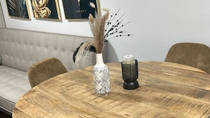 A round wooden table with a vase and candle, surrounded by chairs, in a room with a sofa and framed artwork on the wall. - Room-las3p Acogedor Apartamento Cerca de (Santo Domingo)