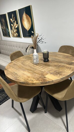 Una mesa redonda de madera con un florero y una vela, rodeada de sillas, en una habitación con un sofá y decoración en la pared.