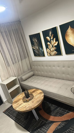 Una sala de estar moderna con un sofá gris, una mesa redonda de madera y tres obras de arte enmarcadas en la pared.