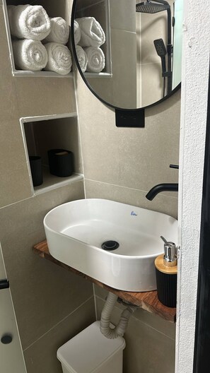 Un baño con lavamanos blanco, un espejo y un perchero con toallas enrolladas.