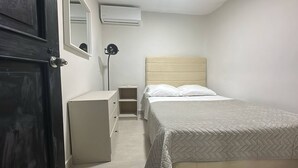 A bedroom with a bed, a dresser, a mirror, and an air conditioning unit. - Room-las3p Acogedor Apartamento Cerca de (Santo Domingo)