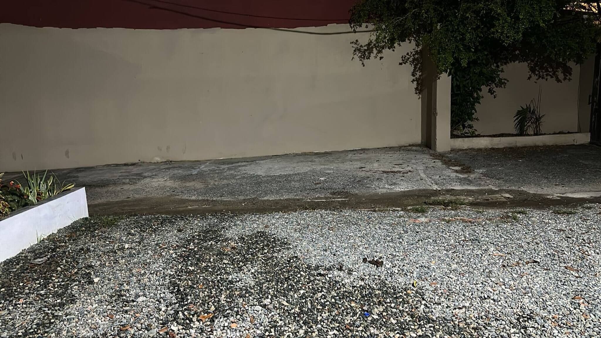 A gravel courtyard with a white planter box, a concrete pathway, and a wall.