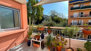 Een balkon met plantenbakken, een witte tafel en een raam.