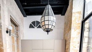 Un espace repas avec une table noire, des chaises blanches, un luminaire suspendu et des murs en pierre.