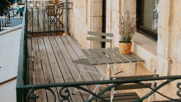 Un balcon en bois avec des rampes en métal, une table et des chaises.
