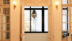 Un portail en arc donne accès à une pièce dont le sol est orné de motifs, qui possède une fenêtre avec une grille décorative et des appliques murales.
