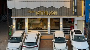 A hotel with a prominent 'HOTEL' sign, a 'MITHILESH' sign, and three parked cars in front.
