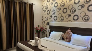 A hotel room with a bed, a ceiling fan, a patterned wall, and a potted plant.