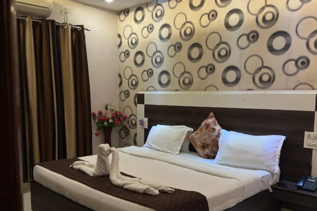 A modern hotel room with a large bed, a nightstand, a wall-mounted air conditioner, and a patterned wall.