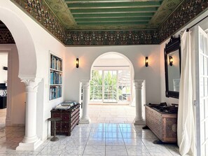 A spacious hallway with a marble floor, a bookshelf, a mirror, and a view through an arched doorway. - Villa Oasis Hammamet (Hammamet)